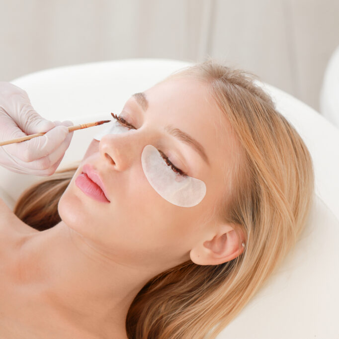 Young woman undergoing procedure of eyelashes dyeing in beauty salon Young woman undergoing procedure of eyelashes dyeing in beauty salon